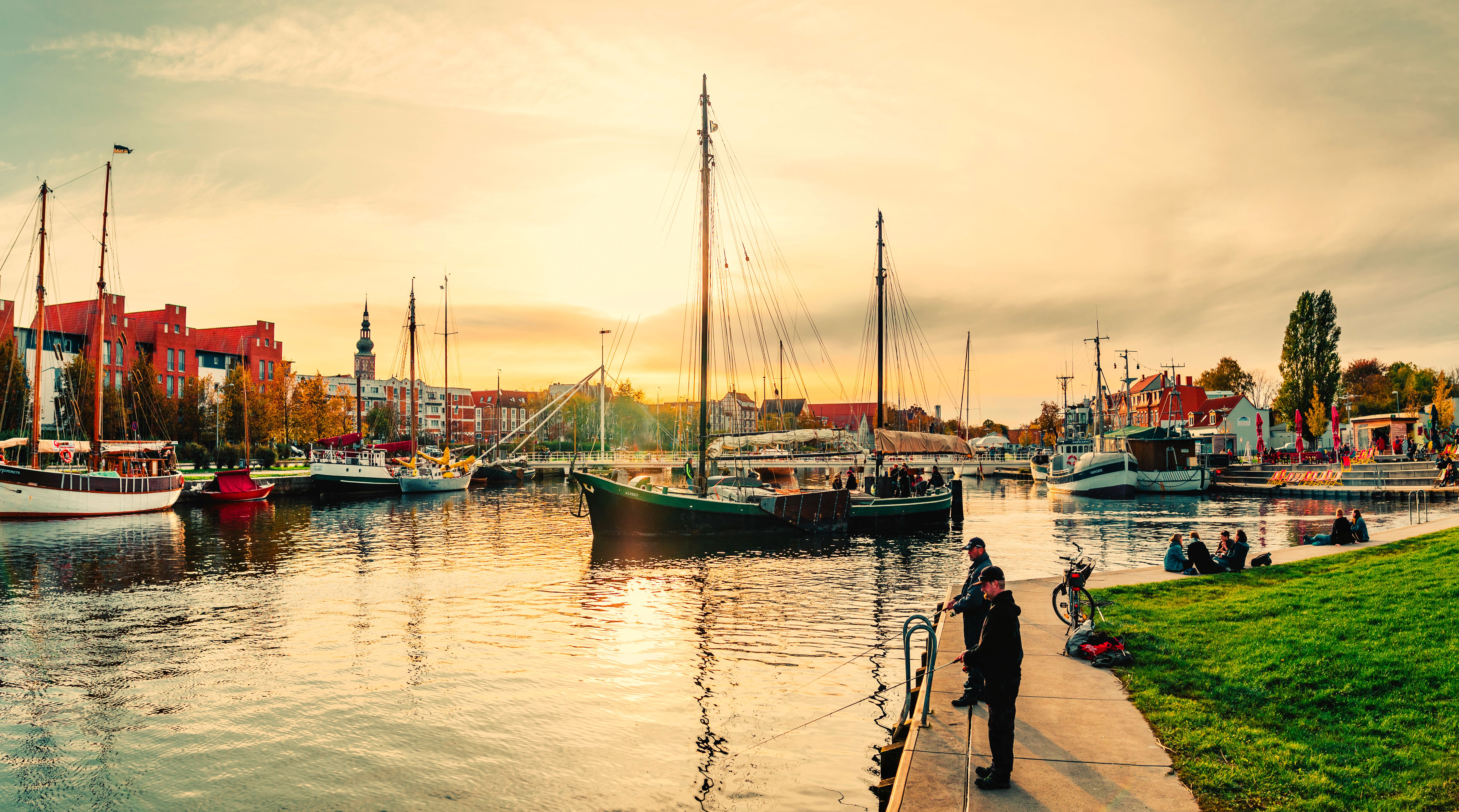 Greifswalder Museumshafen im Sonnenuntergang mit Segelschiff und Angler an der Kaikante