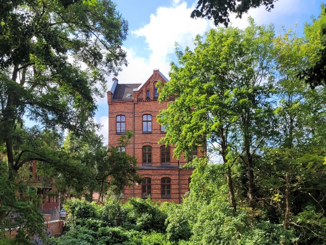 vhs Vorpommern-Greifswald © vhs Vorpommern-Greifswald Außenansicht der vhs Vorpommern-Greifswald. Ein rotes Backsteinhaus inmitten von Bäumen.