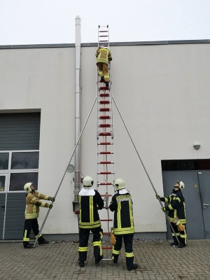 Feuerwehrmänner in Ausrüstung bringen eine Leiter in Stellung, um auf ein Häuserdach zu gelangen