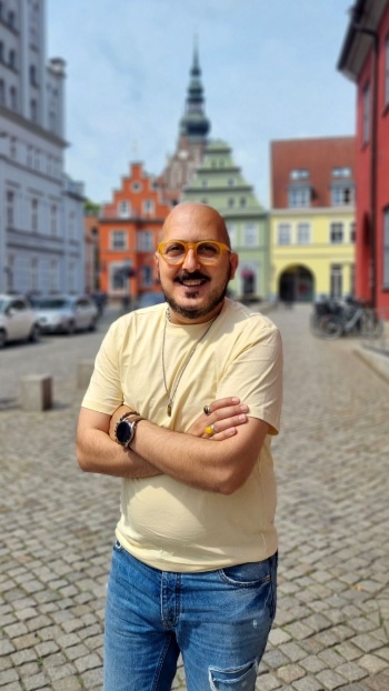 Pressestelle der Universitäts- und Hansestadt Greifswald Avat Ramin Otmishi steht vor dem Greifswalder Rathaus und im Hintergrund ist der Dom St. Nikolai zu erkennen