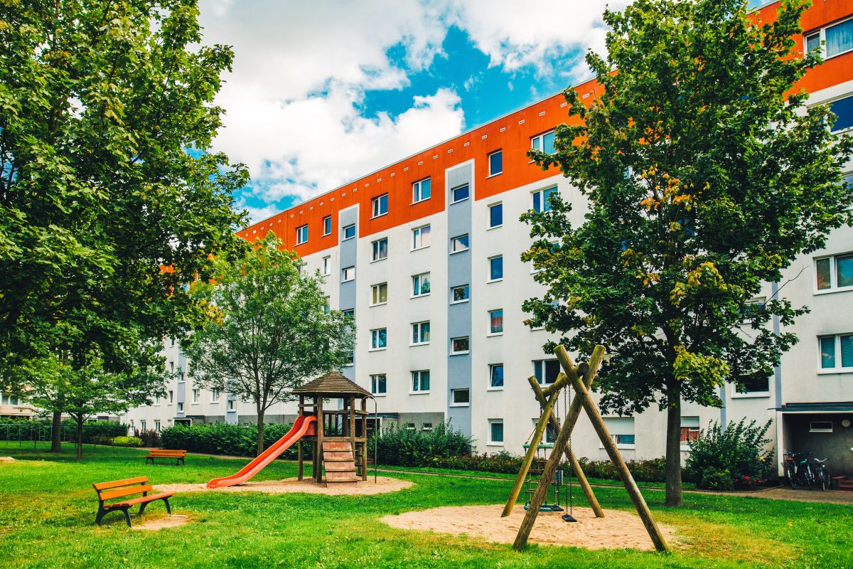 Spielplatz vor einem Gebäude, umgeben von zwei Bäumen