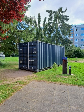 Fahrrad-Selbsthilfe-Werkstatt an der Schwalbe © Quartierskoordination der Universitäts- und Hansestadt Greifswald Ein grauer Seecontainer auf einer Wiese, im Hintergrund steht ein Plattenbau.