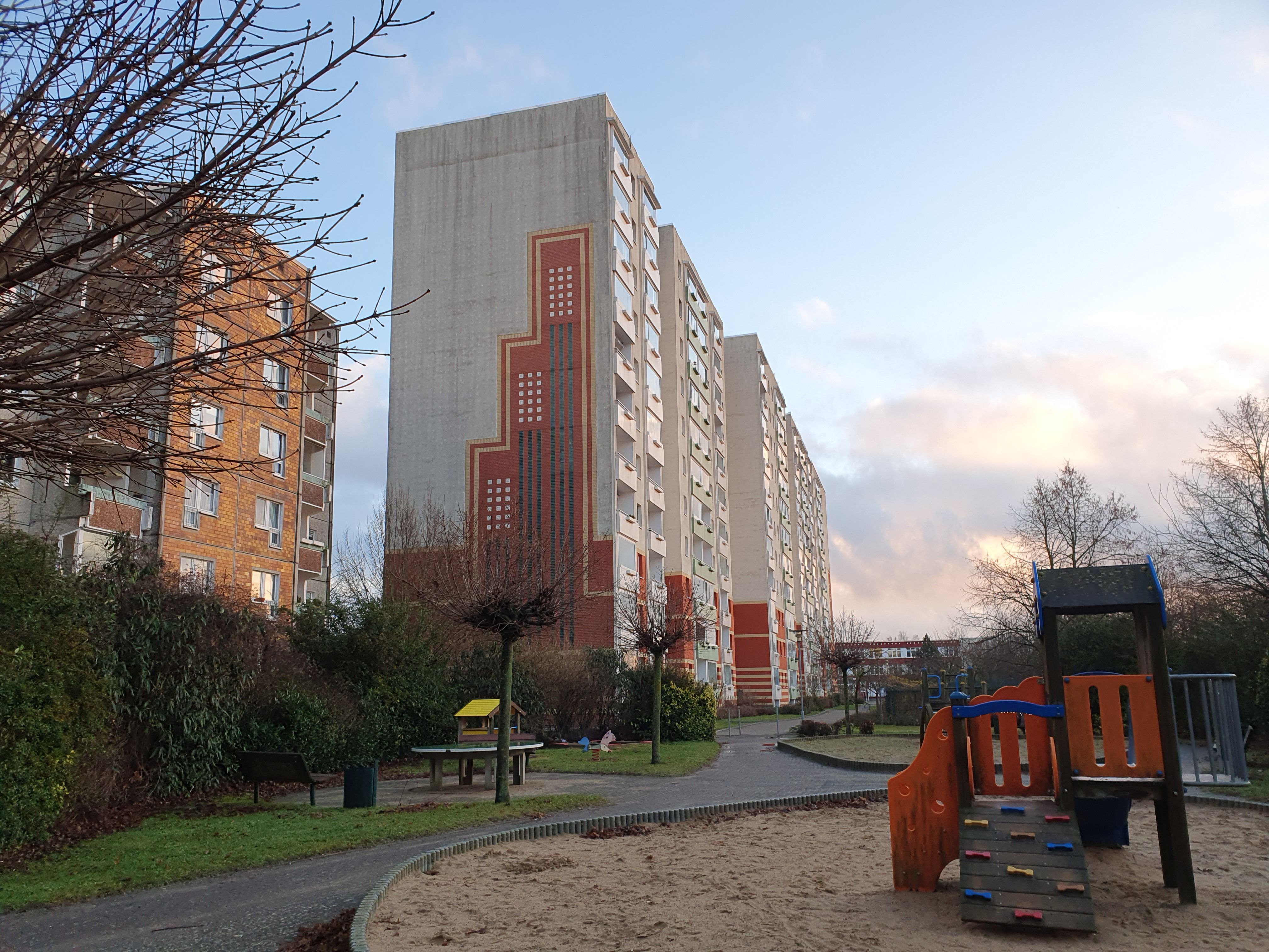 Ein Hochhaus mit einem Spielplatz davor, im Hintergrund Wolken