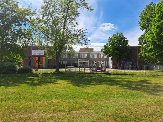 Kita "Regenbogen" © Quartierskoordination der Universitäts- und Hansestadt Greifswald Im Vordergrund eine grüne Wiese mit Bäumen, dahinter ein zweistöckiger Plattenbau mit einem Eingang in der Mitte