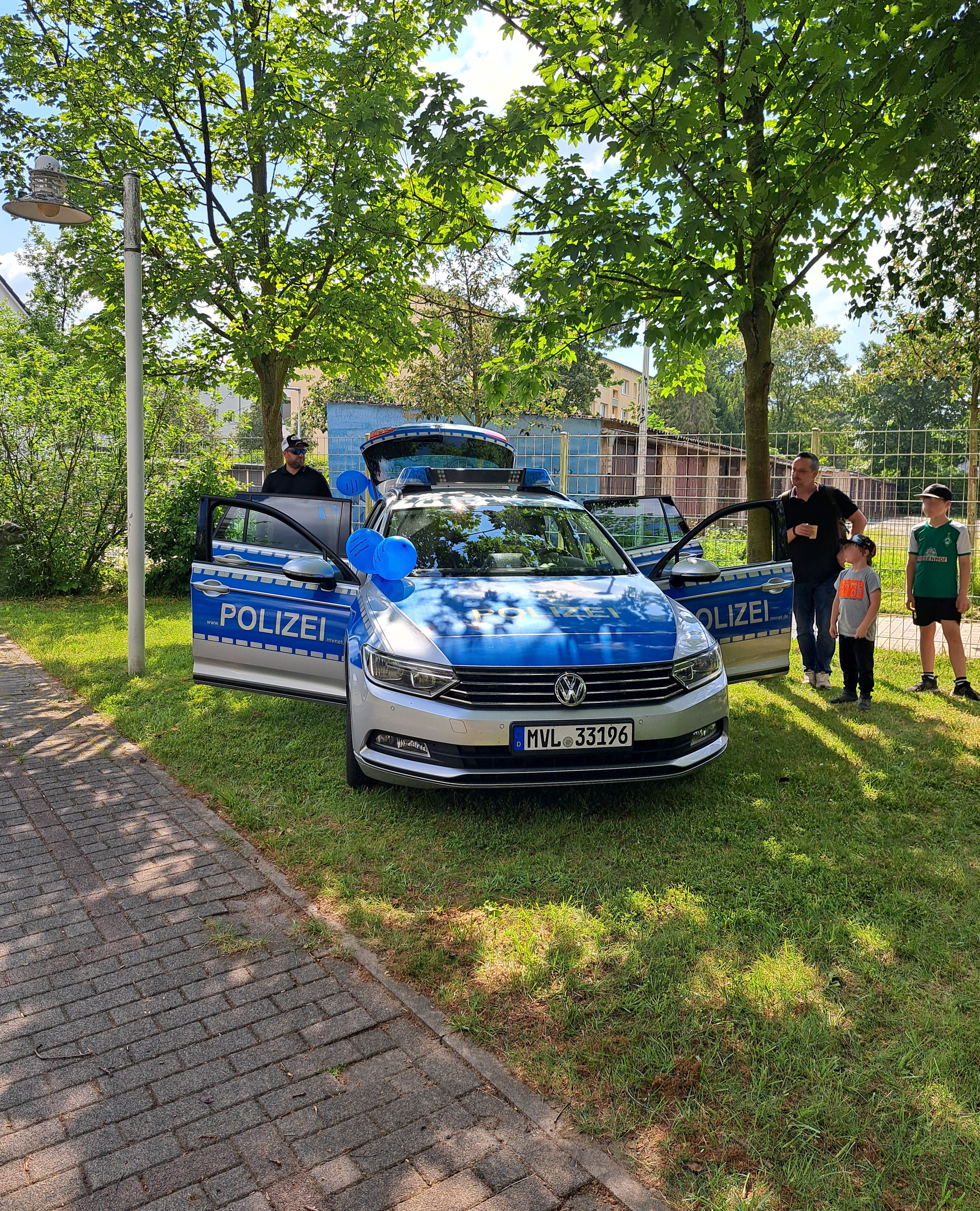 Ein Polizeifahrzeug mit geöffneten Türen steht auf einer Wiese mit Bäumen