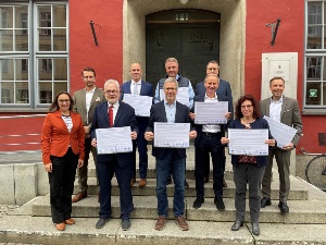 Die Mitglieder des Nachhaltigkeitsbündnisses stehen vor dem Rathaus und halten die unterzeichnete Deklaration hoch. - © Pressestelle Die Mitglieder des Nachhaltigkeitsbündnisses stehen vor dem Rathaus und halten die unterzeichnete Deklaration hoch.