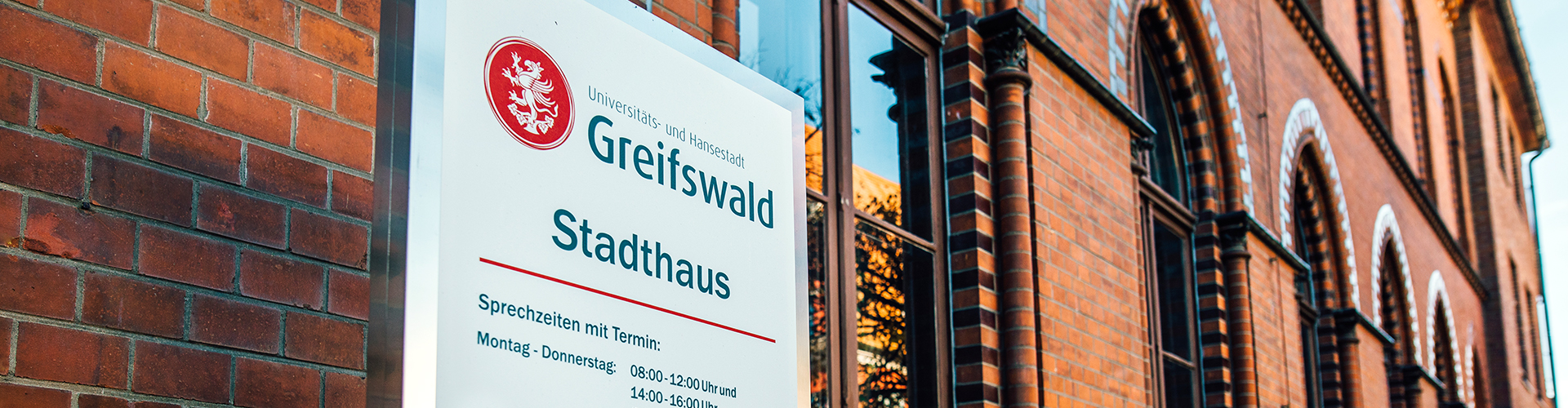 Schild mit Kontakten und Öffnungszeiten des Stadthauses Greifswald