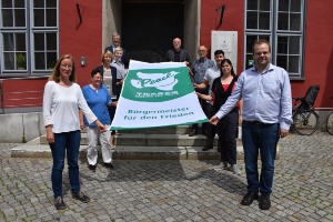 Dr. Fassbinder und Mitglieder der bürgerschaftlichen Gremien entrollen die Flagge