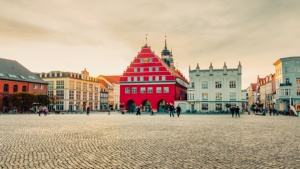 Der Greifswalder Marktplatz. Neben dem roten Rathaus ist eine Apotheke. Vor dem Rathaus steht ein Tasmodell