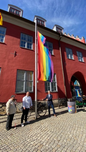 Dr. Fassbinder und Mitglieder von Queer hissen die Regenbogenflagge vor dem Rathaus