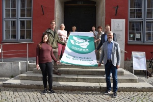 Mitglieder der Bürgerschaft, der OB und Mitarbeitende des Beauftragtenbüros haben die Flagge vor dem Rathaus entrollt.