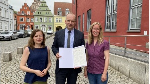 Anna Gatzke, Achim Lerm und Claudia Kowalzyck mit der Charta der Vielfalt vor dem Greifswalder Rathaus - © Pressestelle der Universitäts- und Hansestadt Greifswald Anna Gatzke, Achim Lerm und Claudia Kowalzyck mit der Charta der Vielfalt vor dem Greifswalder Rathaus