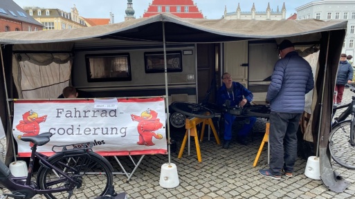 Ein Mitarbeiter der ABS unterhält sich mit einem Bürger in seinem Zelt, vor sich das Fahrrad eingespannt, um es zu codieren
