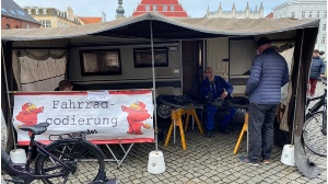 Ein Mitarbeiter der ABS unterhält sich mit einem Bürger in seinem Zelt, vor sich das Fahrrad eingespannt, um es zu codieren - © Pressestelle Ein Mitarbeiter der ABS unterhält sich mit einem Bürger in seinem Zelt, vor sich das Fahrrad eingespannt, um es zu codieren