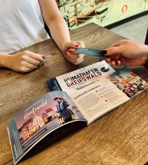 Eine Neubürgerin löst ihren Gutschein aus dem Gutscheinbuch Heimathafen für eine Stadtführung in der Greifswald-Information ein - © Theres Behnke Eine Neubürgerin löst ihren Gutschein aus dem Gutscheinbuch Heimathafen für eine Stadtführung in der Greifswald-Information ein