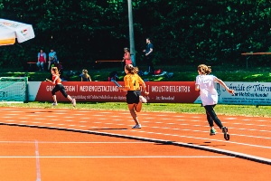 Drei Läuferinnen laufen im Volksstadion einen Staffellauf im Rahmen vom Tag des deutschen Sportabzeichens bei sonnigem Wetter