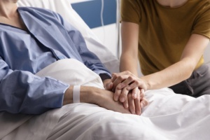 Frau und kranke Mutter halten Hände am Krankenbett