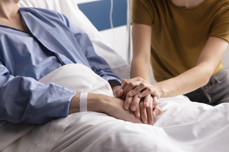 Frau und kranke Mutter halten Hände am Krankenbett