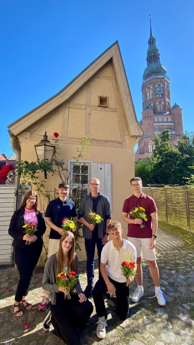 sechs neue Auszubildende stehen vor einem Tor von St. Spritus mit dem Dom im Hintergrund