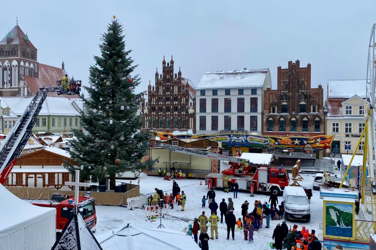 Blick aus dem Rathaus auf dem Marktplatz, auf dem zwei Feuerwehrfahrzeuge mit Drehleitern um den Baum stehen