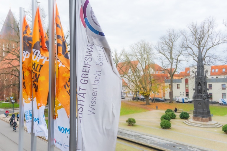 Flaggen zum Orange Day vor dem Hauptgebäude der Universität mit Blick auf das Rubenowdenkmal