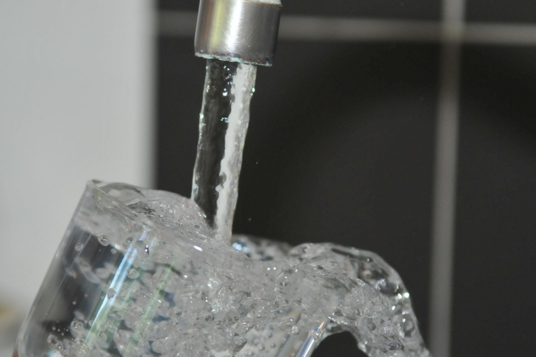 Glas Wasser unter einem laufenden Wasserhahn