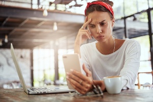 Frau schaut skeptisch auf Smartphone und Laptop