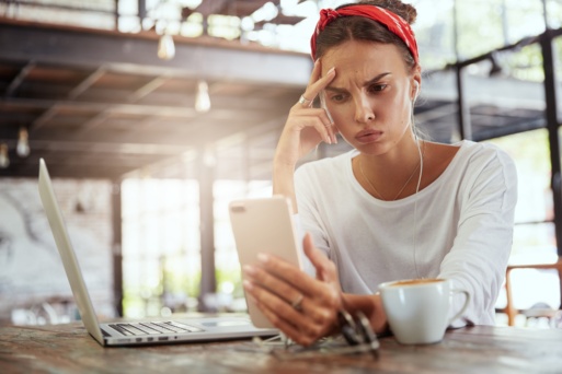 Frau schaut skeptisch auf Smartphone und Laptop
