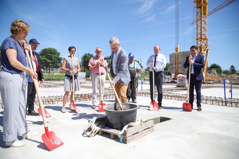 Mehrere Personen betonieren auf der Baustelle die Zeitkapsel ein