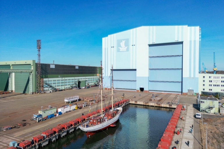 Luftaufnahme der SSS GREIF vor der blauen Werfthalle des Maritimen Industrie- und Gewerbeparks "Volkswerft" Stralsund