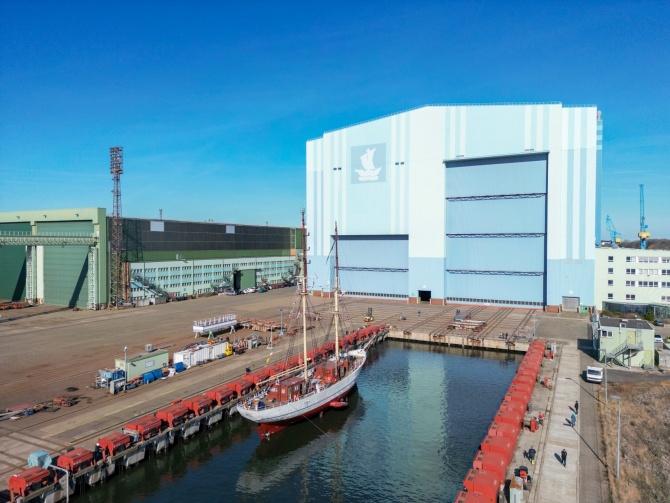 Luftaufnahme der SSS GREIF vor der blauen Werfthalle des Maritimen Industrie- und Gewerbeparks "Volkswerft" Stralsund