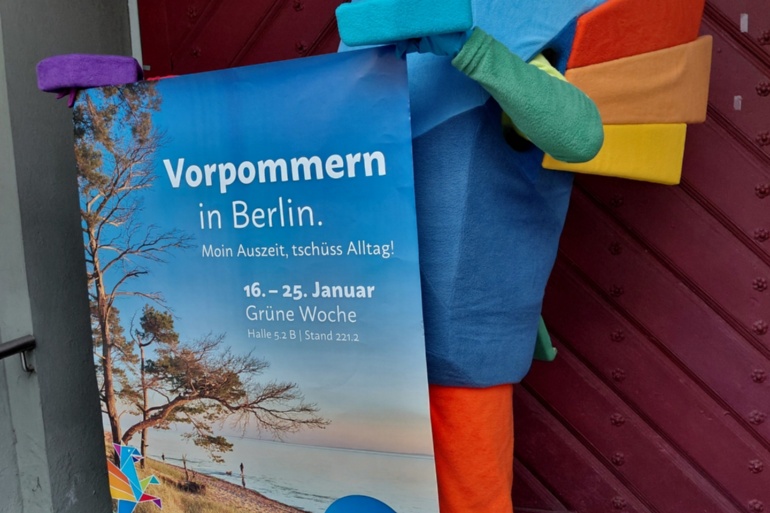 Das Maskottchen Vorpommern-Greif mit einem Veranstaltungsplakat zur Grünen Woche 2026