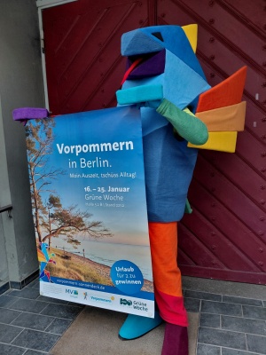 Das Maskottchen Vorpommern-Greif mit einem Veranstaltungsplakat zur Grünen Woche 2026