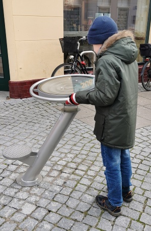 ein Junge steht im Schuhhagen vor einem etwa ein Meter großen Edelstahlfuß mit beweglichem Tellerlabyrinth